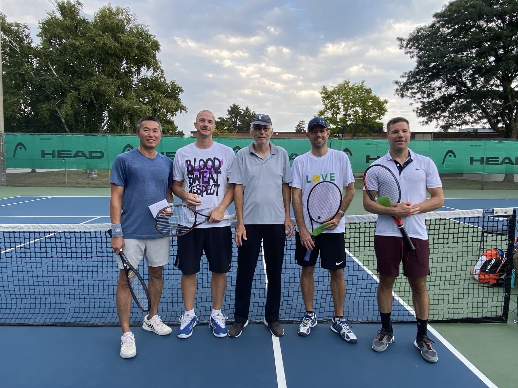 Five adult players, including Bruce, posed at the net at Burlington Tennis Club after a tournament.