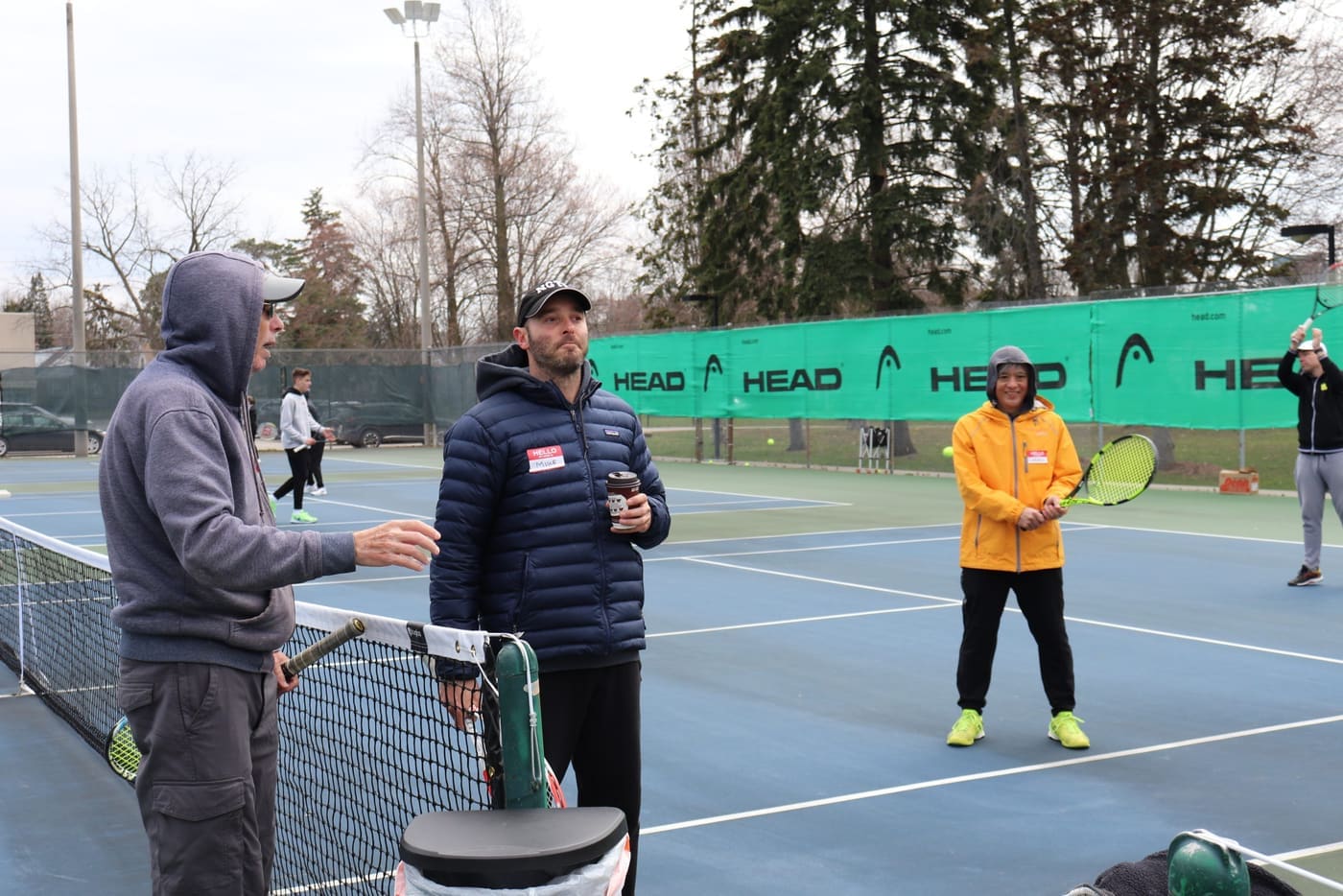 Adult coaches gathered courtside at a winter outdoor tennis event.