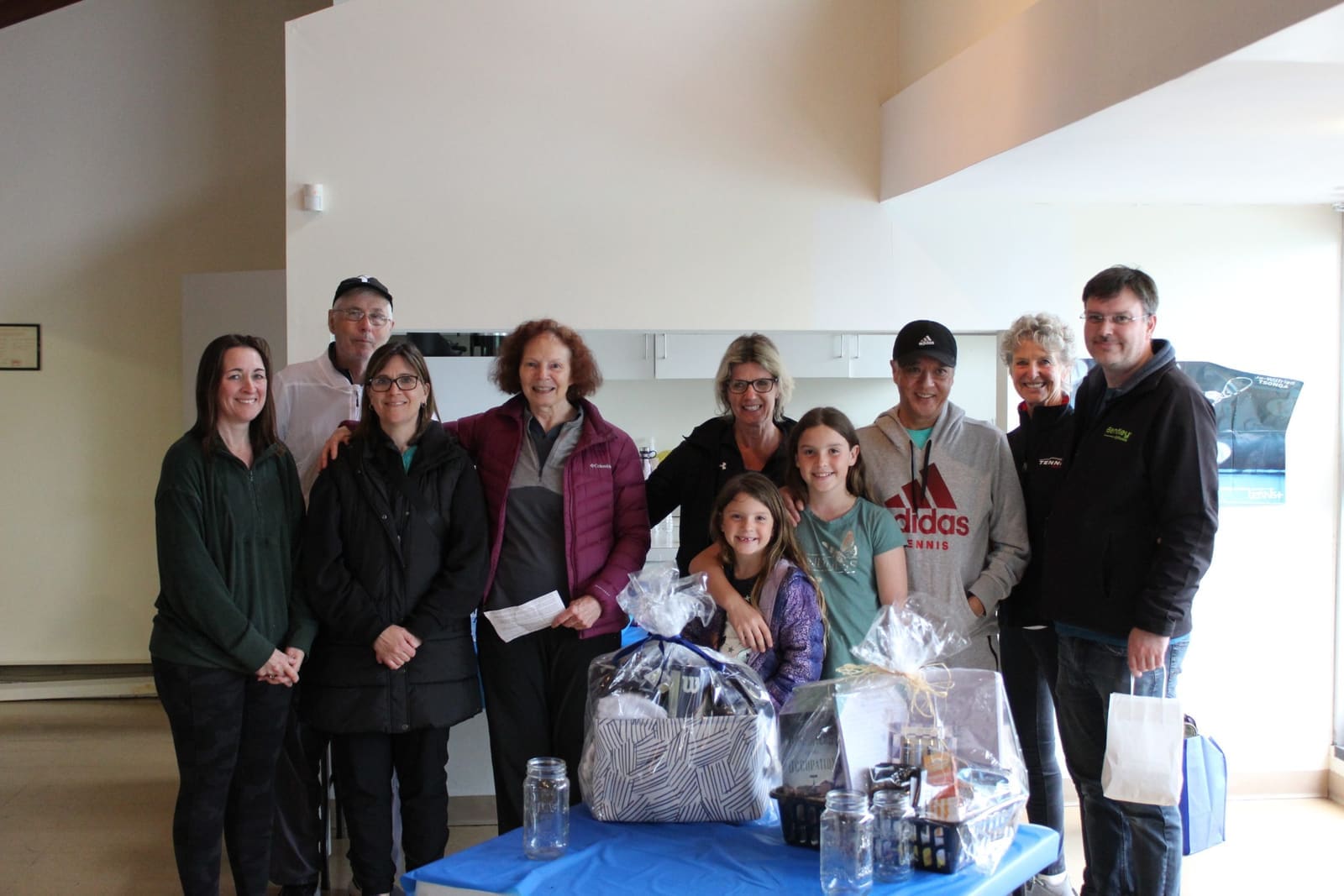 Community celebration at Burlington Tennis Club with members and gift baskets.