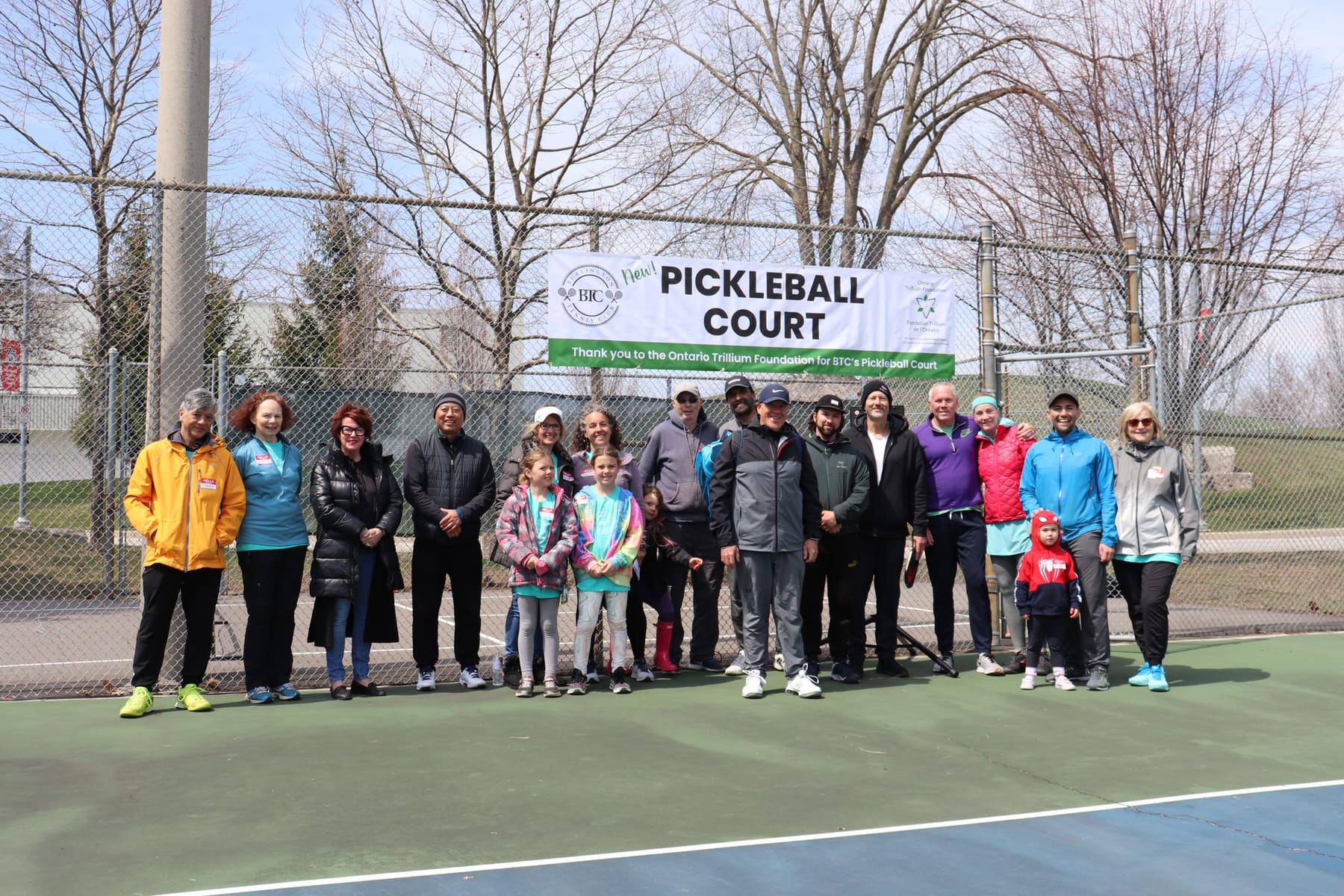 Group photo of BTC members and a few children in front of a large sign reading "New PICKLEBALL COURT" with credit to the Ontario Trillium Foundation.