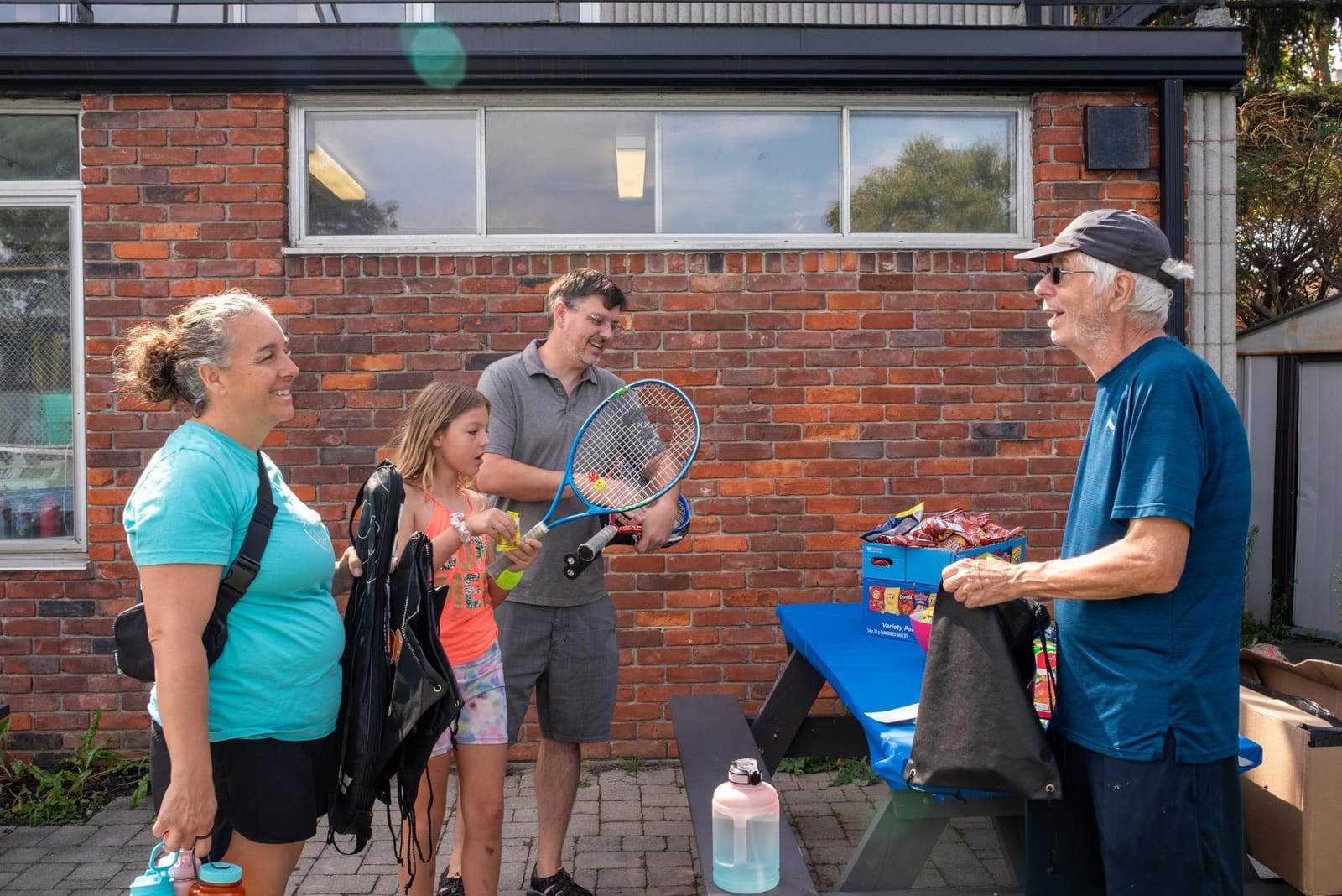 Bruce Cates greeting a family of new juniors with their racquets at Burlington Tennis Club.